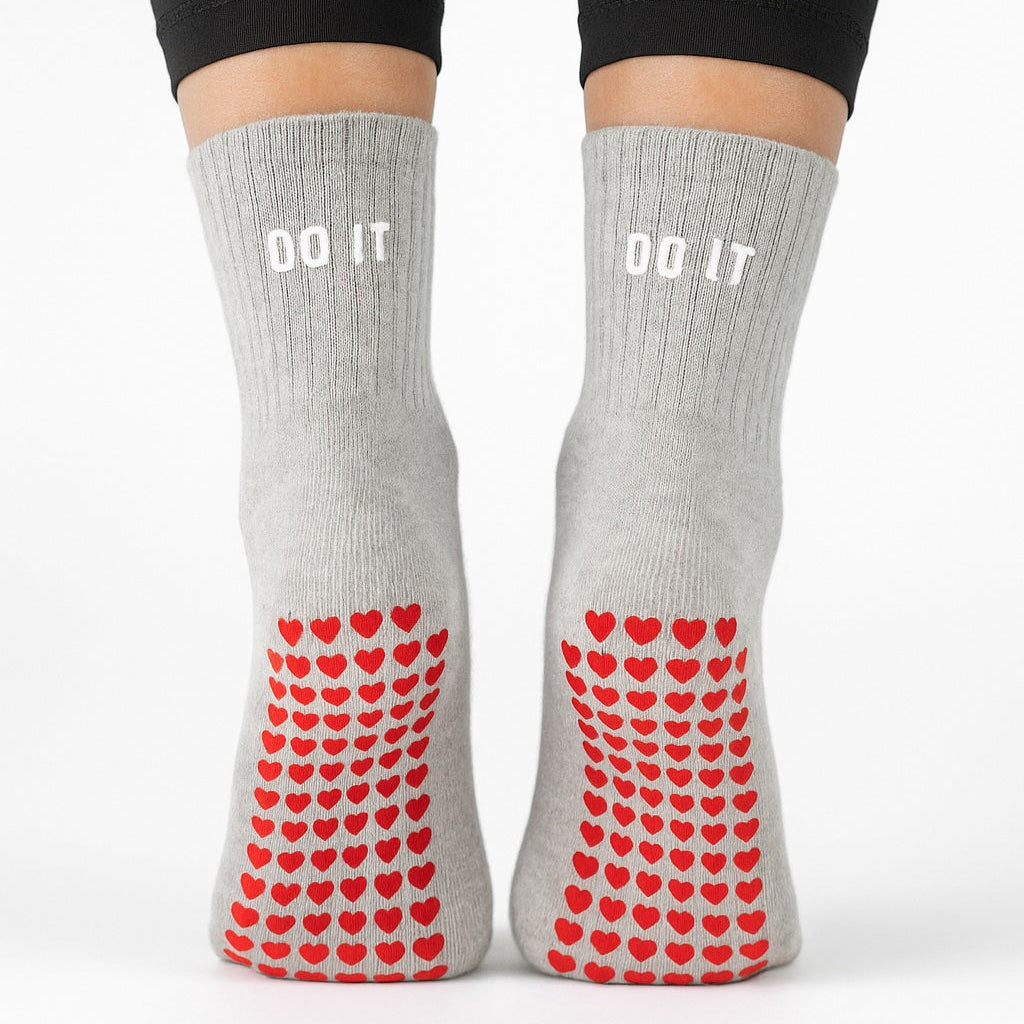 Gray socks with red heart pattern and 'DO IT' text worn with black leggings on a white background